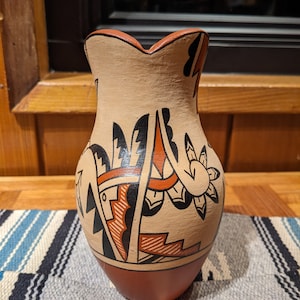 May include: A hand-painted ceramic pitcher with a traditional Southwestern design. The pitcher is decorated with black, red, and white geometric patterns on a tan background.
