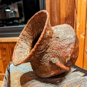 May include: A large, brown, woven basket with a wide, flared opening. The basket has a rough, textured surface and is decorated with small, red dots.