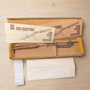 May include: A Rug Crafters speed tufting tool with a wooden handle and metal mechanism, housed in a cardboard box. Includes an instruction sheet with the text 'RC RUG CRAFTERS SPEED TUFTING TOOL INSTRUCTIONS' and a small white paper receipt.