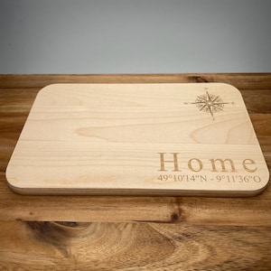 May include: A wooden chopping board with a compass design and the text "Home 49°10'14"N - 9°11'36"O"