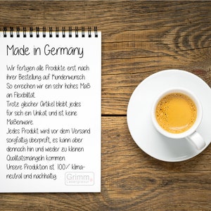 Op de afbeelding: Een wit notitieboek met een zwarte spiraalbinding op een houten oppervlak. Het notitieboek heeft de tekst "Made in Germany" in het zwart bovenaan. Het notitieboek bevat een lijst met opsommingstekens in het Duits over het productieproces van het bedrijf en zijn inzet voor duurzaamheid.
