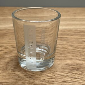 Op de afbeelding: Een helder glazen shotglas met het woord "Drink Name" gegraveerd aan de zijkant.
