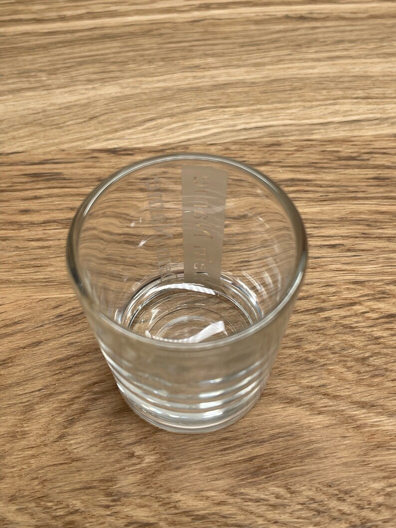 Op de afbeelding: Een helder glazen shotglas met een verhoogd, getextureerd ontwerp rond de bodem. Het glas heeft een wit label met de tekst "AUSTRIA" erop gedrukt.