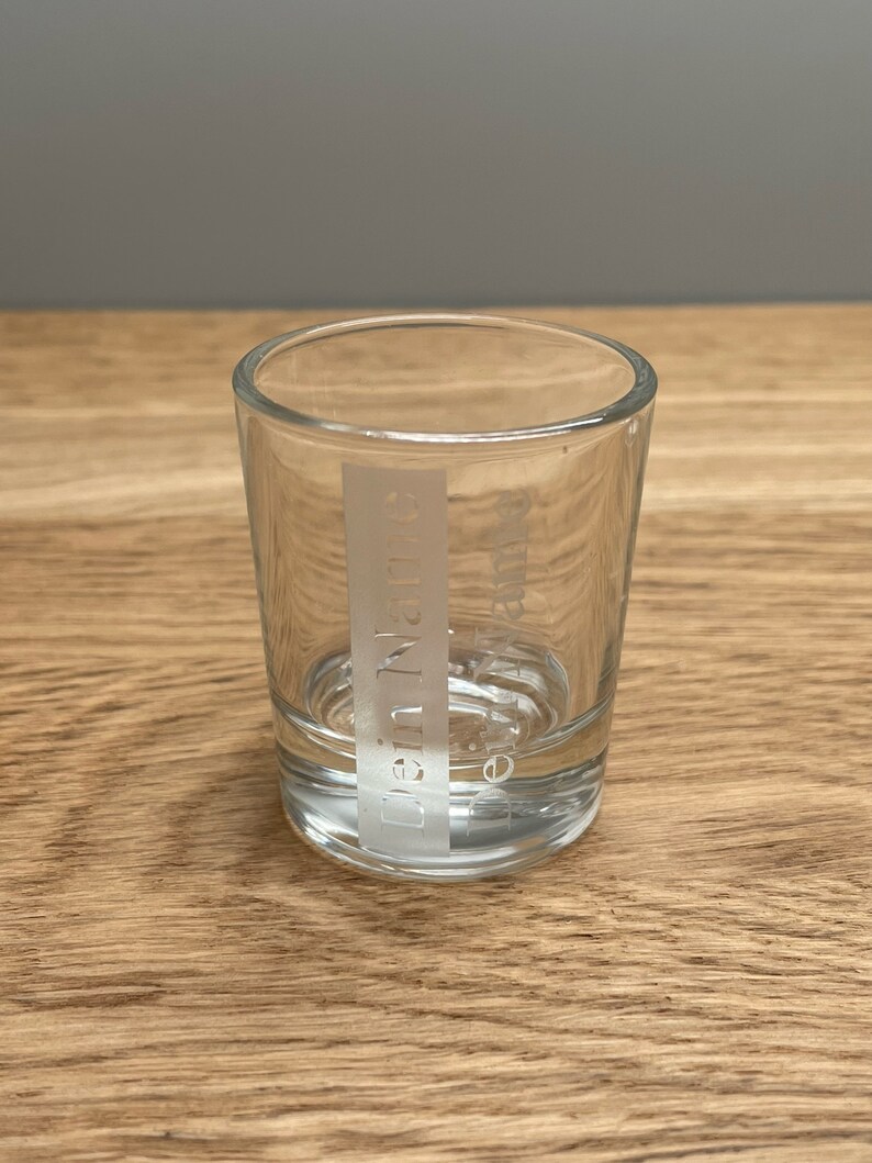 Op de afbeelding: Een helder glazen shotglas met het woord "Dennys" erop gegraveerd.