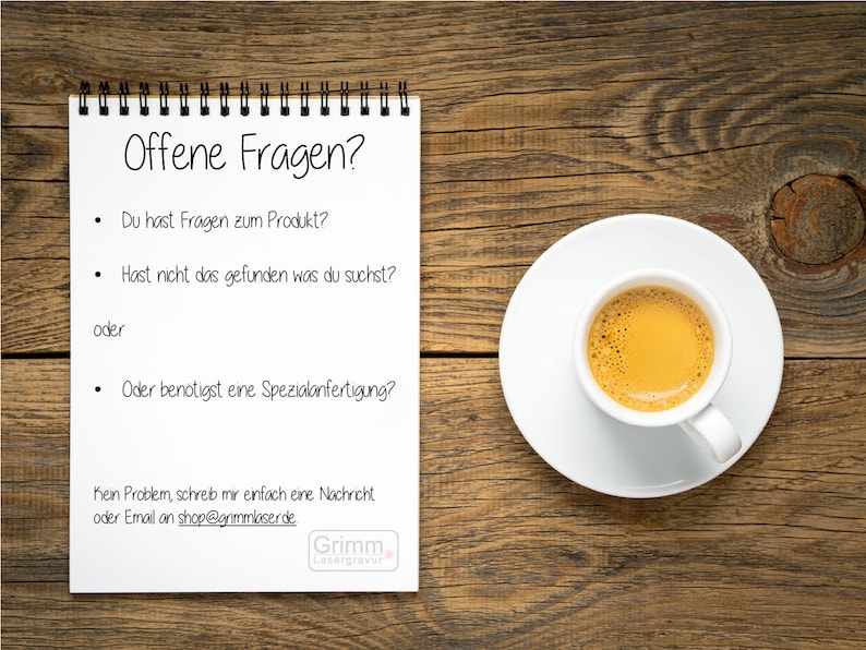 Op de afbeelding: Een wit notitieboekje met een zwarte spiraalbinding op een houten oppervlak. Het notitieboekje heeft bovenaan de tekst "Offene Fragen?" en een lijst met vragen in het Duits. De tekst onderaan het notitieboekje luidt "Kein Problem, schreib mir einfach eine Nachricht oder Email an shop@grimmlaserde.de". Er is een witte kop koffie met een bruine vloeistof en een witte schotel op het houten oppervlak.