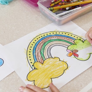 May include: A child is colouring a rainbow with a green crayon. The rainbow is drawn on a white sheet of paper with a yellow cloud and a butterfly. The rainbow is coloured in brown, green, blue, and yellow.