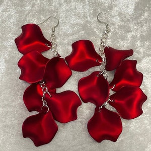 May include: A pair of long, dangling earrings with a silver chain and multiple red petal-shaped charms.