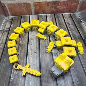 May include: A collection of yellow and gray pixelated toy blocks and a sword, arranged on a dark wood surface. The blocks are in various shapes, resembling a character or structure from a video game. The sword is also pixelated.