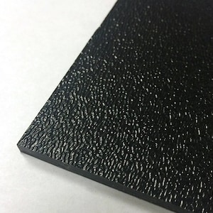 May include: Close-up of a black, textured material with a rough, speckled surface. The material has a slightly reflective quality, and the edges are clean and sharp. The background is white.