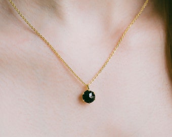 Può includere: Una collana con catena d'oro e ciondolo in pietra nera.