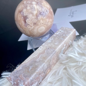 Puede incluir: Una esfera de ágata rosa y blanca y una losa de ágata rectangular con un patrón de remolino. El ágata es una piedra natural con un patrón único y hermoso.
