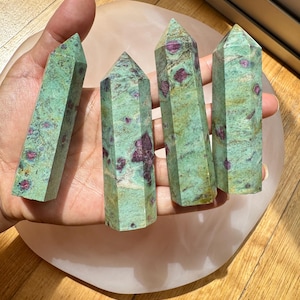May include: Four green and red ruby zoisite crystal points, also known as ruby in zoisite, on a pink surface. The points are smooth and polished.