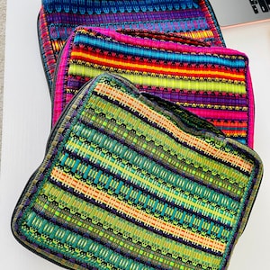 Pode incluir: Três bolsas com zíper coloridas com um padrão listrado. As bolsas são feitas de tecido tecido e têm um zíper preto. As bolsas estão empilhadas uma em cima da outra.