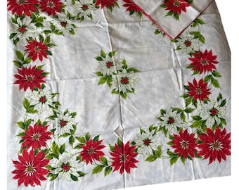 May include: A white square tablecloth and a matching square napkin featuring a printed pattern of red and white poinsettia flowers with green leaves. The fabric has a smooth texture and the napkin has a thin red border along the edges.
