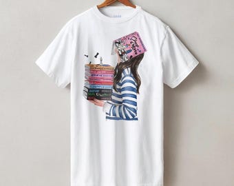 May include: A white short-sleeve t-shirt featuring a graphic illustration of a person wearing a blue and white striped sweater, holding a stack of colorful books, with a pink book titled Check & Mate covering their face and chess pieces.