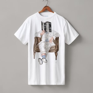 以下が含まれることがあります： 白い半袖Tシャツ。ストライプのスーツを着た人物が茶色の肘掛け椅子に座り、BABELというタイトルの本を顔の前に掲げているグラフィックイラストが描かれています。人物は青い靴下と白黒の靴を着用しています。