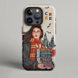 Puede incluir: Funda de teléfono con una ilustración en acuarela de una persona con gafas y bufanda, sosteniendo una pila de libros. La funda tiene un fondo crema con murciélagos y un diseño de castillo. La palabra "CRÉE" está impresa en la parte superior.