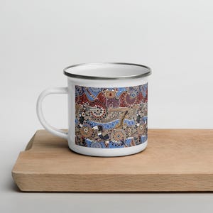 May include: White enamel mug featuring a colorful Aboriginal art design. The artwork includes stylized animals like a koala and birds, with a pattern of dots and lines in shades of blue, red, and brown. The mug has a silver rim and a white handle.