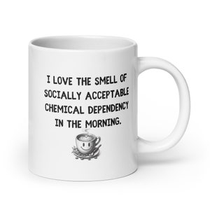 May include: White ceramic coffee mug with the text "I LOVE THE SMELL OF SOCIALLY ACCEPTABLE CHEMICAL DEPENDENCY IN THE MORNING." A small illustration of a smiling coffee cup is below the text.