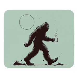 May include: A black and white illustration of a Bigfoot walking with a steaming cup of coffee in his hand. The background is a light blue color with a white circle in the upper left corner.