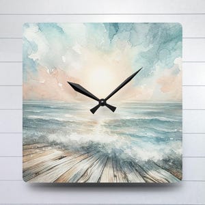 May include: Square clock featuring a watercolour painting of a seascape with a wooden jetty in the foreground. The sky is a soft blue and pink with clouds. The ocean is a deep blue with white waves. The clock hands are black.