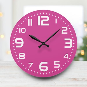 Op de afbeelding: Een ronde roze klok met witte cijfers en zwarte wijzers. De klok heeft een eenvoudig ontwerp en is perfect voor elke kamer.