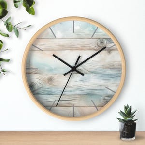 May include: Circular wall clock with a light wood frame. The clock face displays a watercolour design of light blue and beige wooden planks. Black clock hands and minimalist hour markers. A decorative accent for any room.