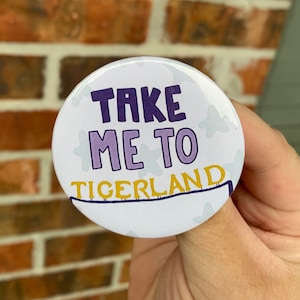 May include: A white button with purple and yellow text that reads "Take Me To Tigerland". The button has a white background with small white stars.