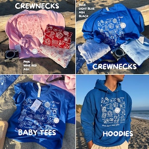 K&ouml;nnte beinhalten: Eine Auswahl an Crewnecks, Baby-T-Shirts und Hoodies in verschiedenen Farben, darunter Rosa, Blau und Aschgrau. Jedes Kleidungsst&uuml;ck zeigt ein wei&szlig;es Grafikdesign mit dem Text "DTMF" und anderen Illustrationen. Eine Kamera und gefaltete Bandanas sind ebenfalls zu sehen.
