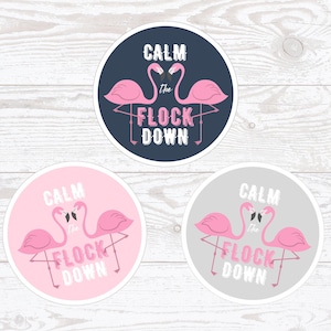 May include: Three round stickers with pink flamingos and the text "Calm the Flock Down". The stickers are on a white wood background. The stickers are in three different colours: navy blue, pink, and grey.