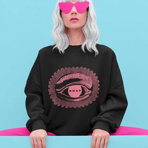 May include: A black sweatshirt with a pink eye graphic and the text "NMAP" inside the eye. The model is wearing pink heart-shaped sunglasses and has white hair.