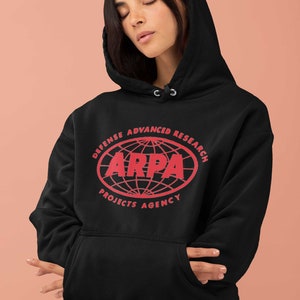 Peut inclure: Sweat-shirt à capuche noir avec un graphisme rouge du logo de la "Defense Advanced Research Projects Agency", également connue sous le nom de DARPA, représentant un globe avec le texte "ARPA" au centre.