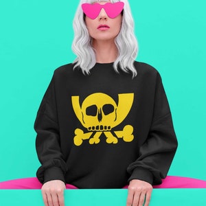 May include: A black sweatshirt with a yellow skull and crossbones graphic. The model is wearing pink heart-shaped sunglasses and has white hair.
