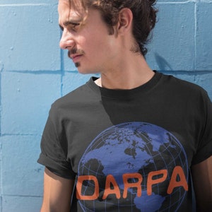 May include: A black t-shirt with a blue and black globe graphic and the word "DARPA" in orange letters.