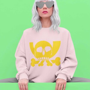 May include: A pink sweatshirt with a yellow skull and crossbones graphic. The model is wearing the sweatshirt and has white hair and heart-shaped sunglasses.