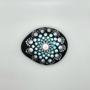 Handpainted dot mandala stone in a geometric floral pattern on a black background with iridescent details. Perfect hostess gift!