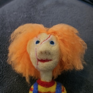 May include: A hand-felted doll with orange hair, blue eyes, and a red and yellow striped shirt. The doll has a stitched-on scar on its face.