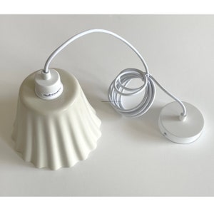 May include: White ceramic pendant light fixture with a ruffled shade and a white cord. The fixture has a white ceiling plate with two small holes.