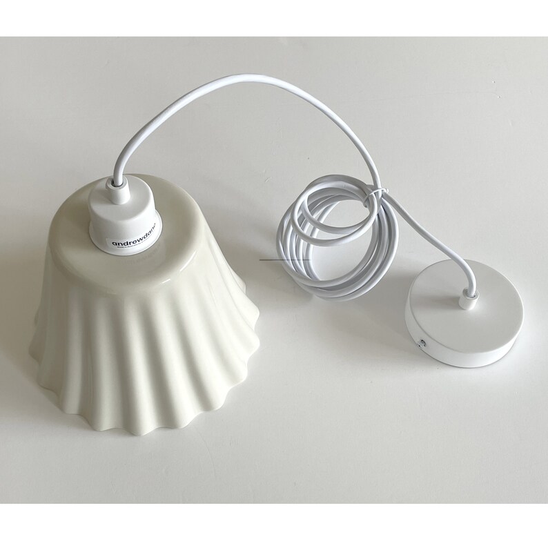 May include: White ceramic pendant light fixture with a ruffled shade and a white cord. The fixture has a white ceiling plate with two small holes.
