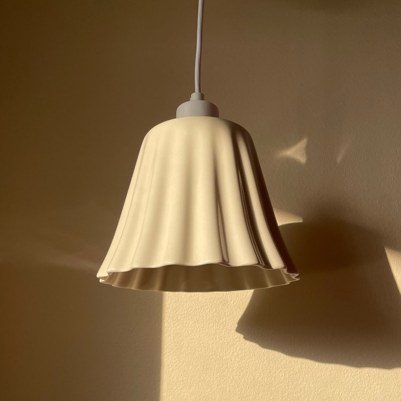 May include: A white ceramic pendant light fixture with a ruffled, bell-shaped shade.