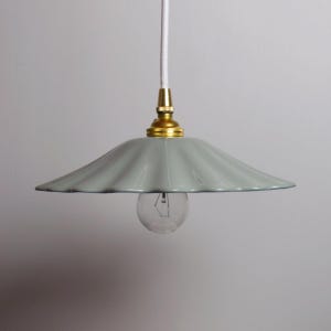 Op de afbeelding: Lichtblauwe hanglamp met geschulpte rand, messing fitting en heldere gloeilamp. De lamp hangt aan een wit snoer. De lamp heeft een retro, vintage design.