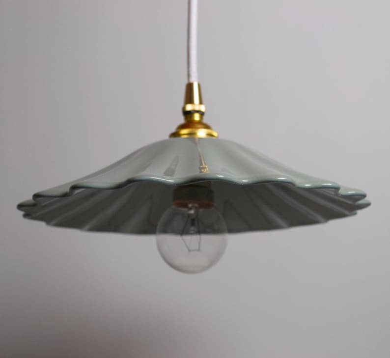 Op de afbeelding: Een grijze hanglamp met geschulpte rand, een goudkleurige basis en een heldere gloeilamp. Het licht hangt aan een wit snoer. De armatuur heeft een zachte, gedempte grijze kleur.
