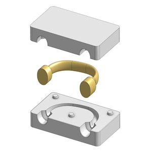 May include: A 3D rendering of a brass-colored handle with a curved design, positioned between two gray rectangular molds. The molds have curved cutouts to accommodate the handle's shape. The handle has cylindrical ends.
