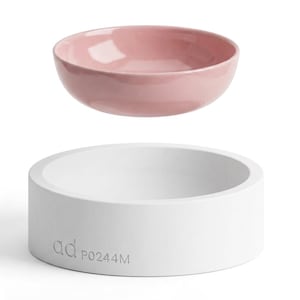 Könnte beinhalten: Eine rosa Keramikschale schwebt über einem weißen, zylindrischen Sockel. Auf der Seite des Sockels steht der Text "ad P0244M". Die Schale hat eine zarte rosa Farbe und scheint leer zu sein. Der Hintergrund ist weiß.