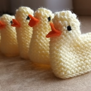 May include: Five knitted yellow ducklings with orange beaks and black eyes. The ducklings are lined up in a row.