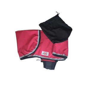 Op de afbeelding: Een roze regenjas voor honden met reflecterende bies en een zwarte trekkoordtas. De regenjas heeft een label met de tekst "Zip a Pup" met een rood hart.