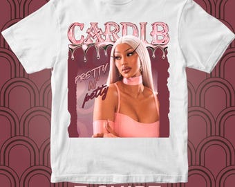 May include: White t-shirt featuring a graphic of Cardi B with the text "CARDI B" in pink dripping letters. The image also includes the words "Pretty N Petty" and the text "T-SHIRT" with the Instagram handle @ayastatements.