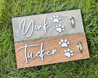May include: Two wooden signs with paw prints and hooks. The top sign is grey and says "York". The bottom sign is brown and says "Tucker".