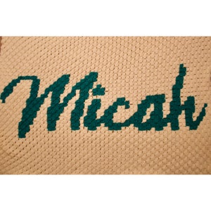 Peut inclure: Une couverture au crochet avec le nom "Micah" écrit en fil de couleur vert sarcelle.