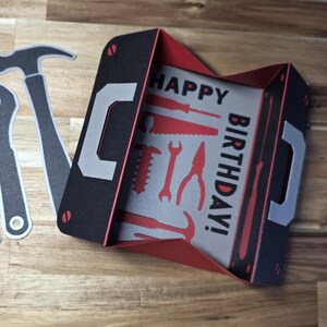 May include: A black and red birthday card shaped like a toolbox, with the words "HAPPY BIRTHDAY!" and tool illustrations. Includes cut-out tool shapes: pliers, wrench, and hammer.